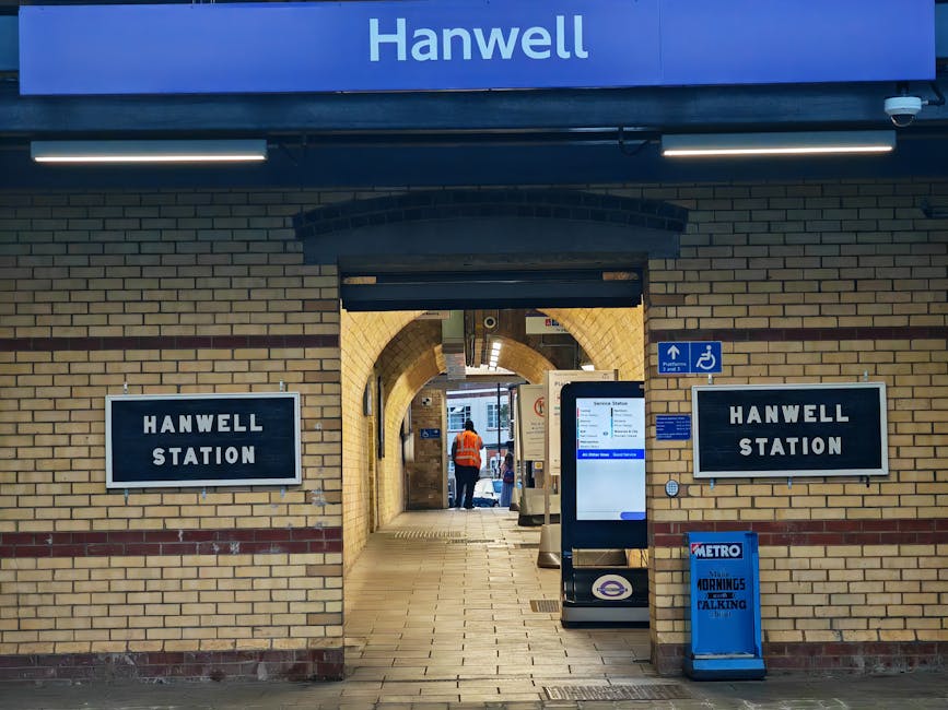 Inside Stockwell Station showing a stairwell with metallic handrails and nearby escalators. The ceiling is unfinished, with visible wiring and fluorescent lighting fixtures. The walls are painted with
